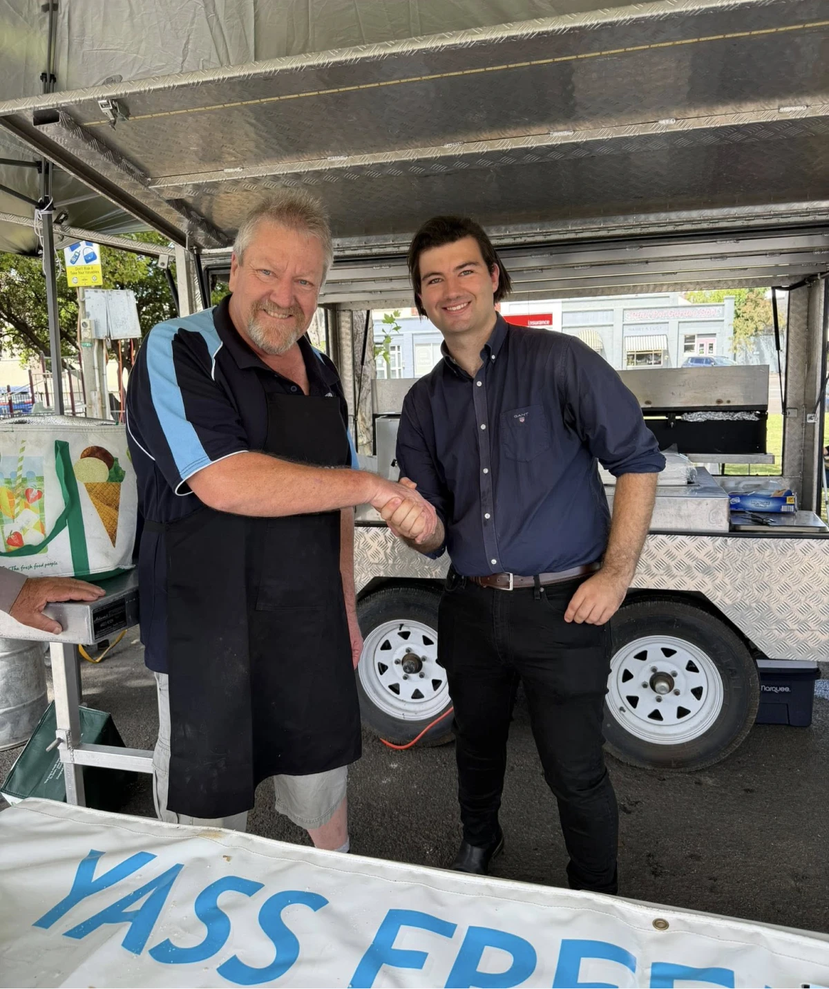 Two men shaking hands at outdoor stall.