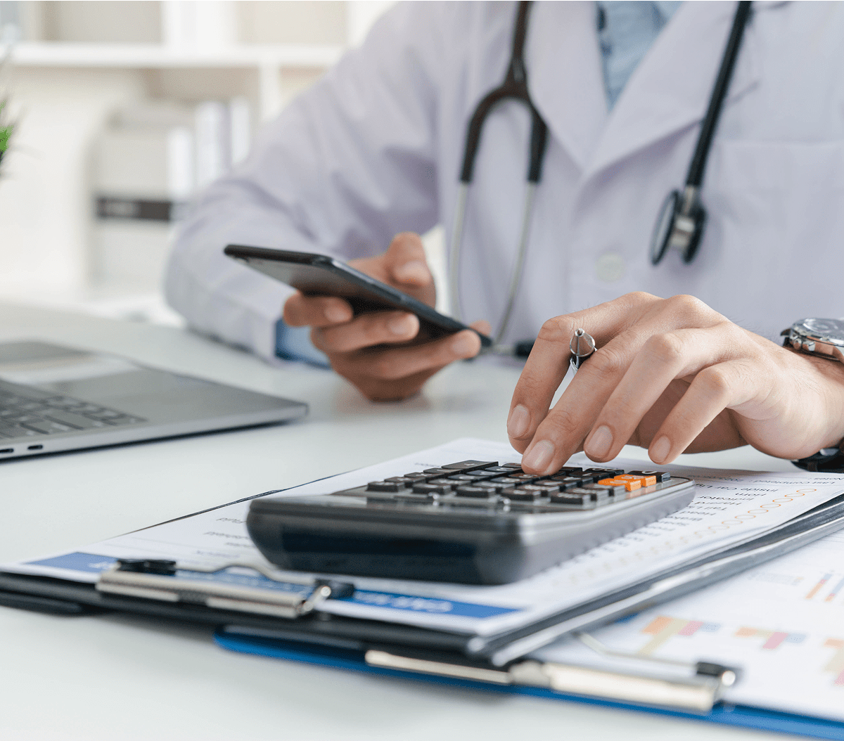Doctor using calculator and smartphone at desk.