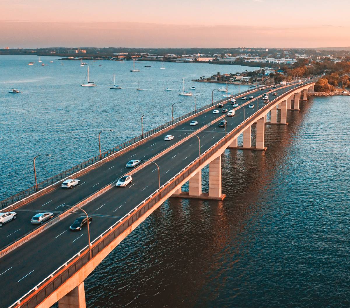 Aerial view of a bridge with cars crossing over calm blue water at sunset